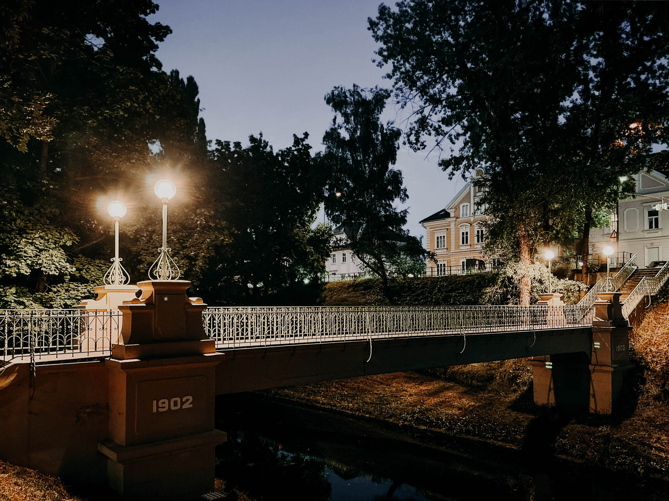 Beleuchtete Brücke mit Stadtmobiliar und Hausfassaden bei Nacht