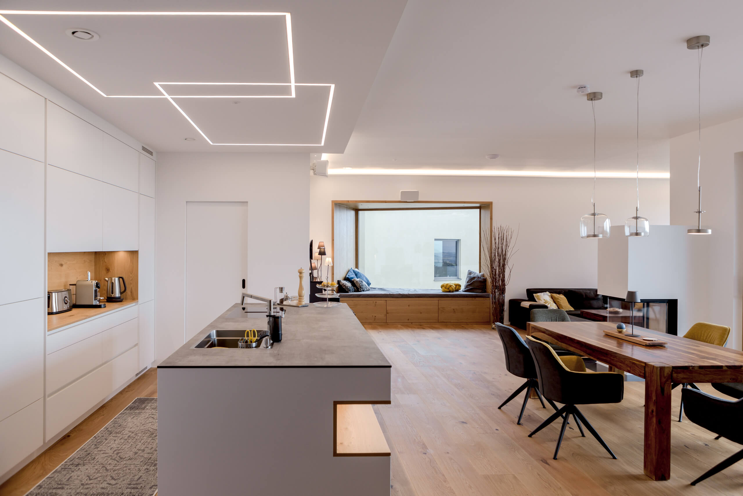 Modernes Wohnzimmer mit integrierter Küche und Sitznische – Lichtplanung für Privatkunden.