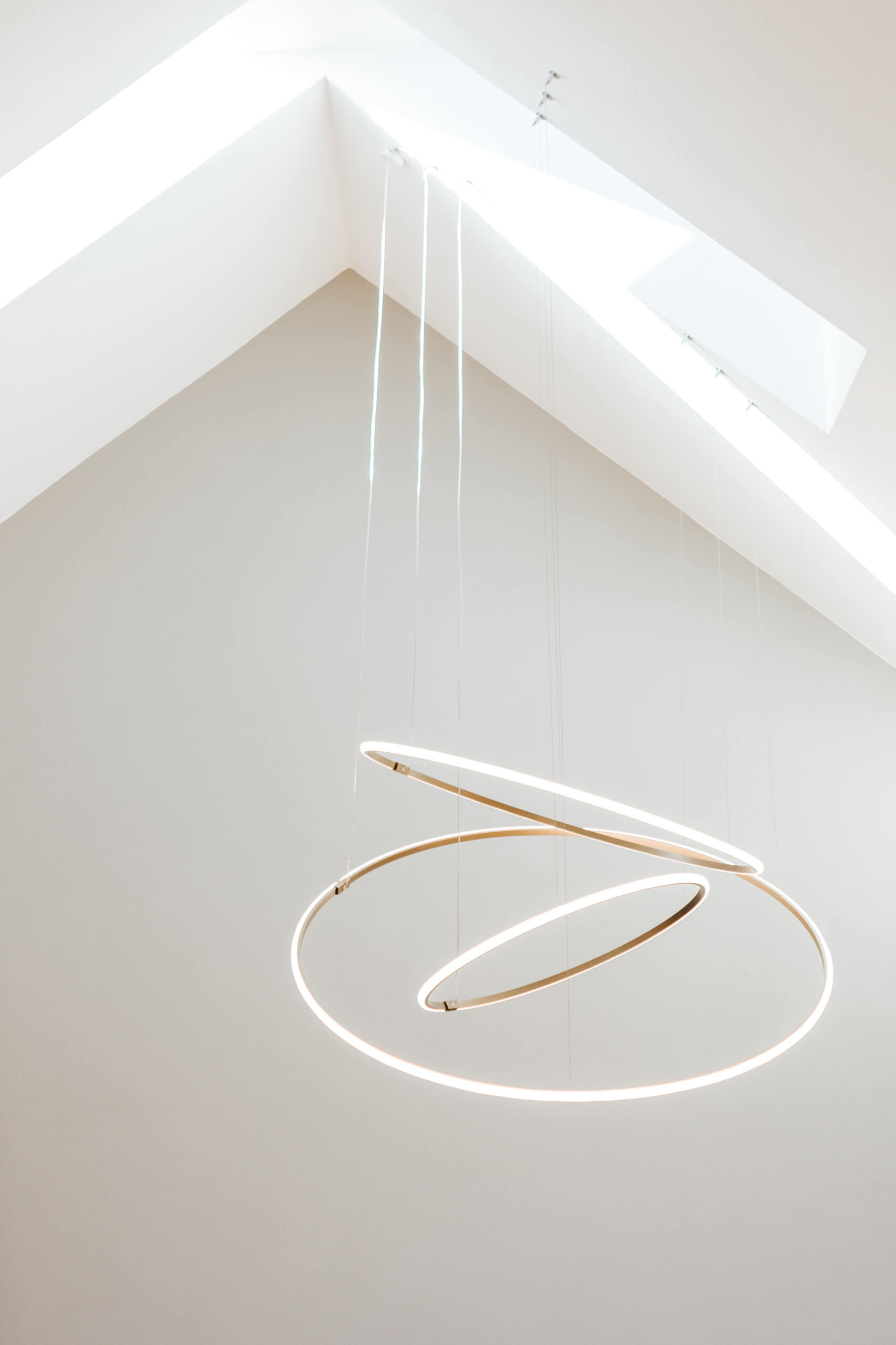 Moderne Ring-Hängeleuchte in einem hellen Raum mit schrägen Deckenfenstern – Lichtplanung