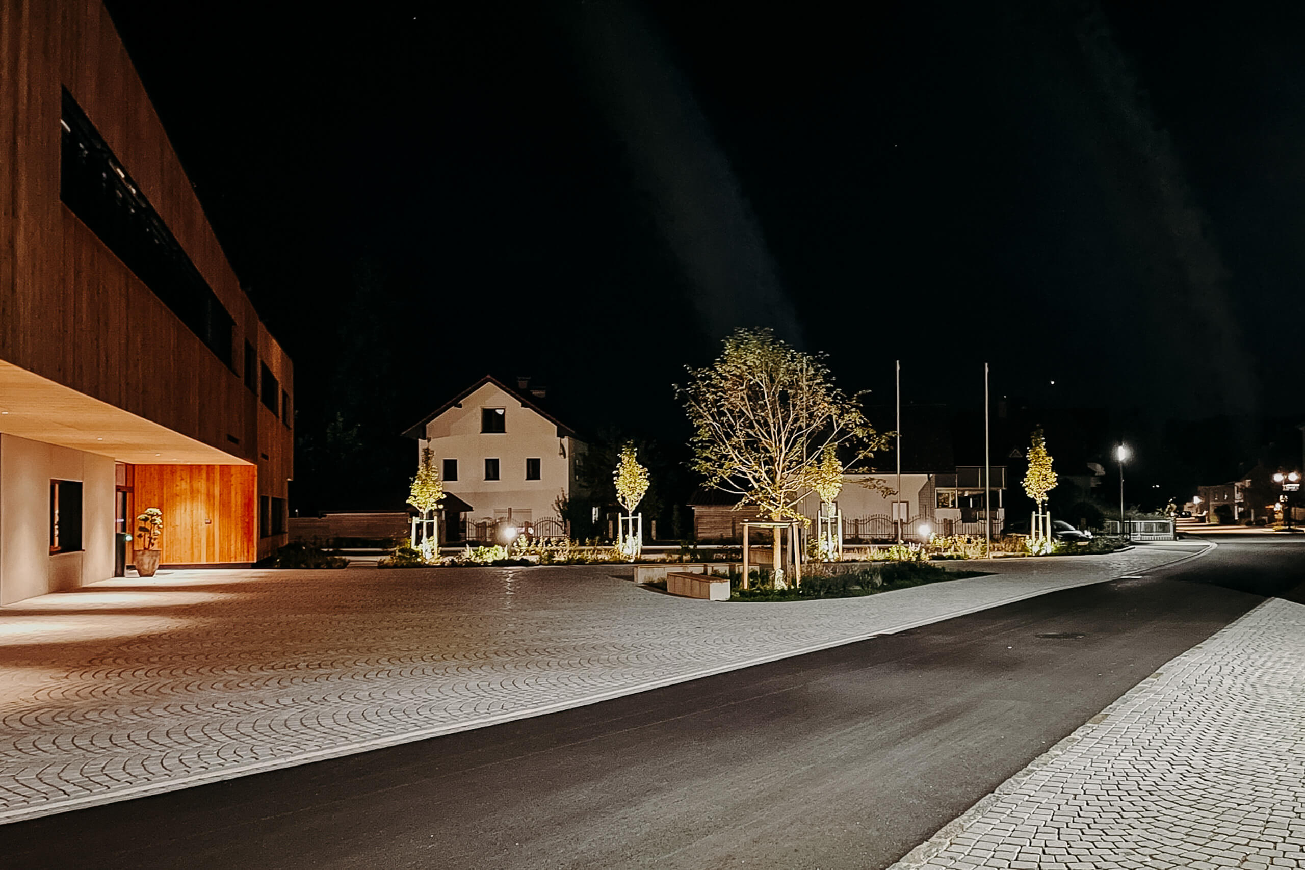 Moderne Stadtmobiliar-Beleuchtung mit Fassadenanstrahlung und Bäumen